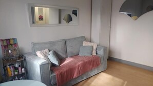 A living room with a grey sofa, a red throw blanket, a small round table, a mirror, and a cabinet. - Lovely studio close to Champs Elysées (Paris)