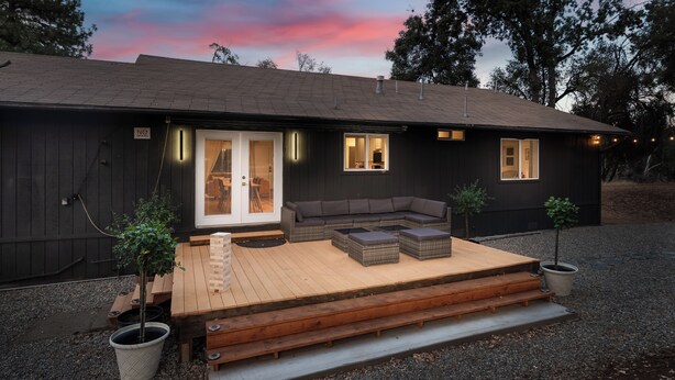 Una casa moderna con terraza de madera, un sofá gris y dos plantas en macetas.