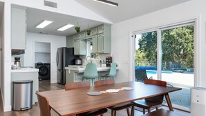 Cocina moderna con comedor, lavadora y un amplio ventanal con vistas a árboles.