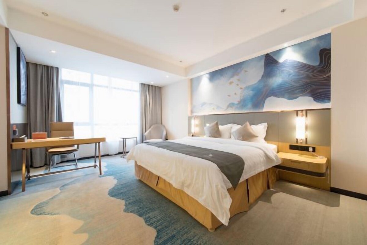 A modern hotel room with a large bed, a desk, and a chair.
