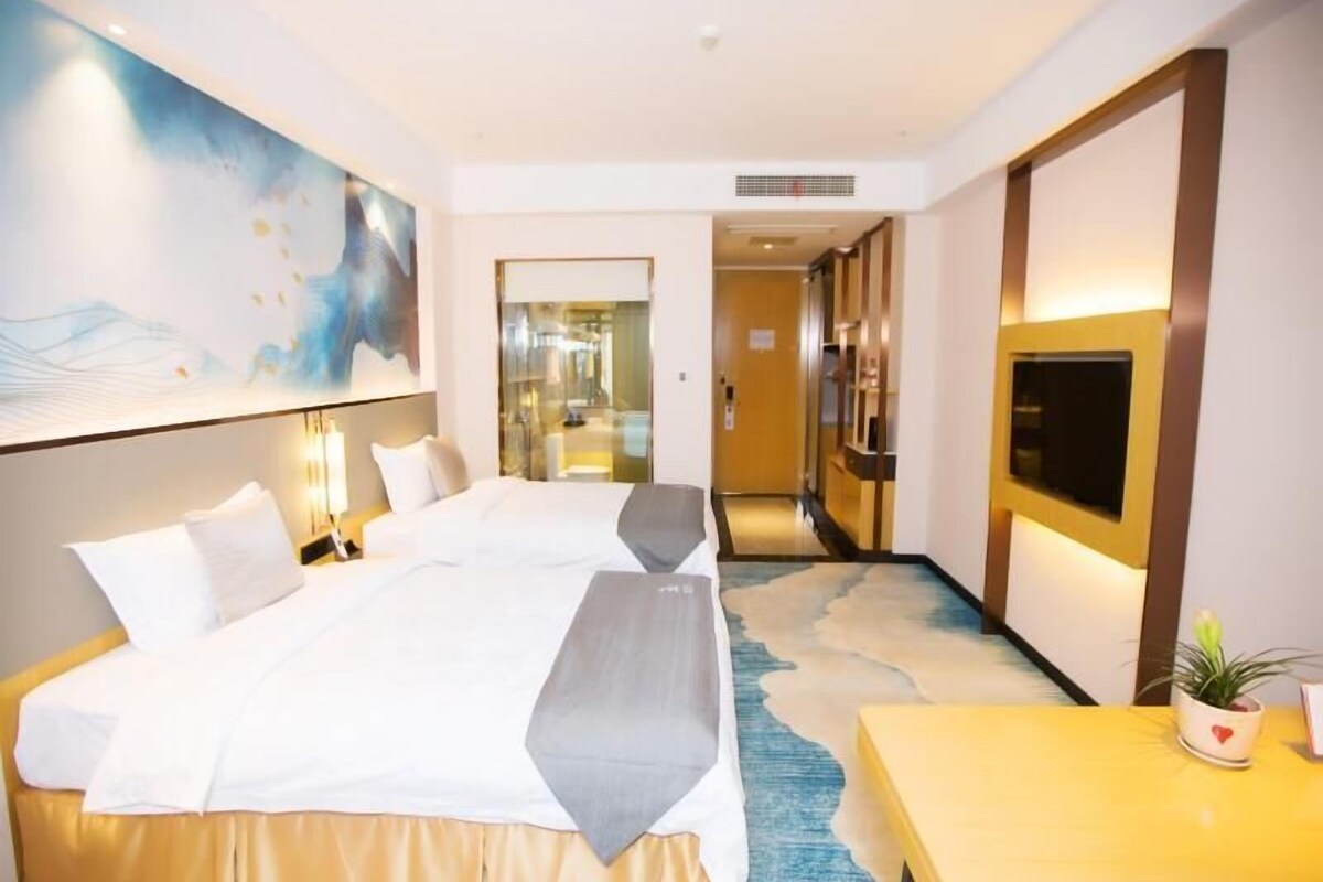 A hotel room with a large bed, a desk, a TV, and a painting on the wall.