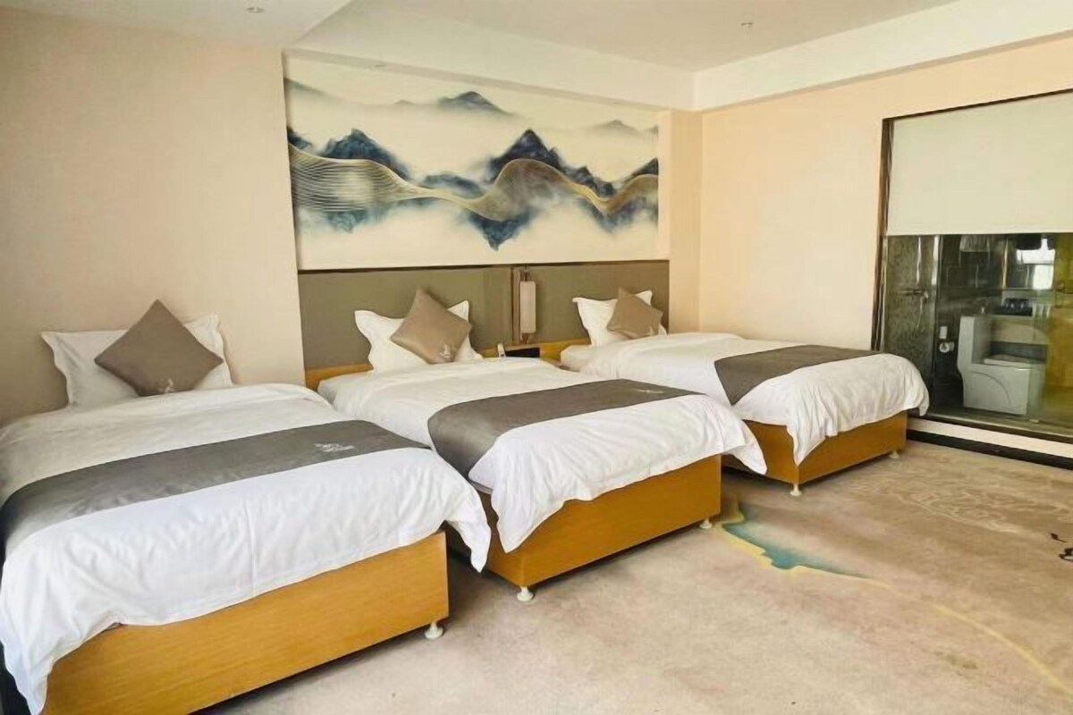 A hotel room with three beds, a large painting on the wall, and a large window.