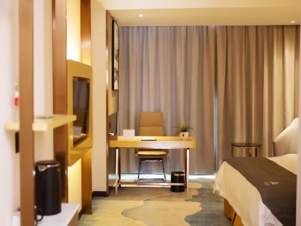 Habitación de hotel con una cama, un escritorio con silla, una mesita, una planta en maceta y una cortina.