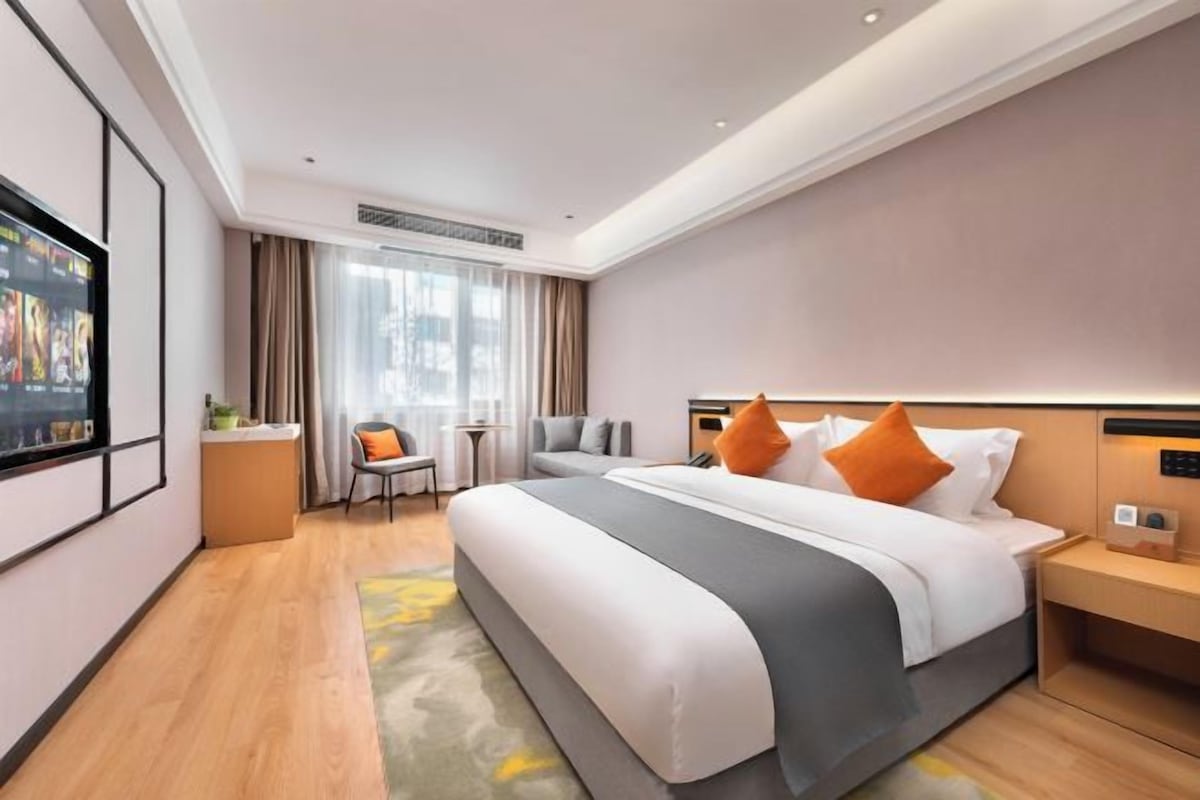 Moderni hotellihuone, jossa on suuri sänky, työpöytä, tuoli ja televisio.