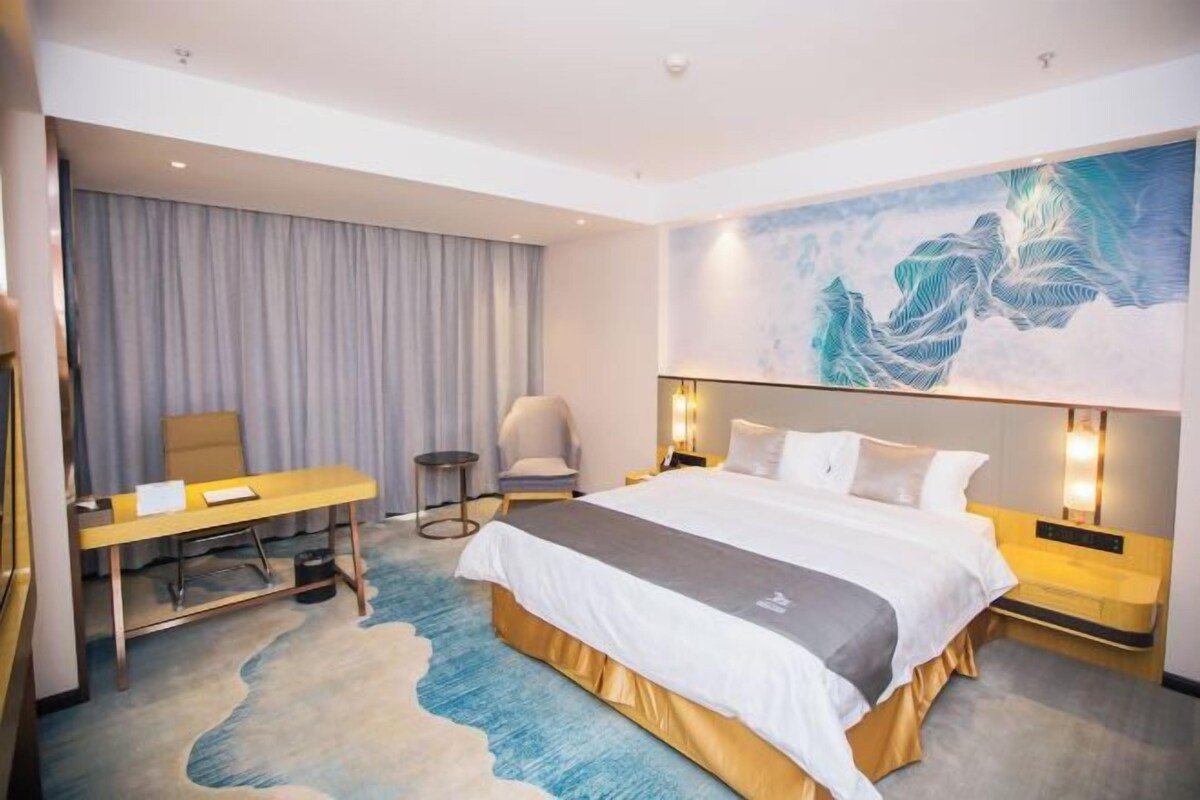 A hotel room with a bed, a desk, a chair, and a large painting on the wall.