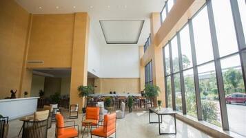 A spacious lobby with high ceilings, large windows, and a mix of seating areas including chairs and tables.