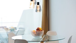 A modern dining area with a glass table, white chairs, and a bowl of fruit.