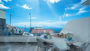 A balcony with a table set for breakfast, overlooking a coastal view with houses and a clear sky.