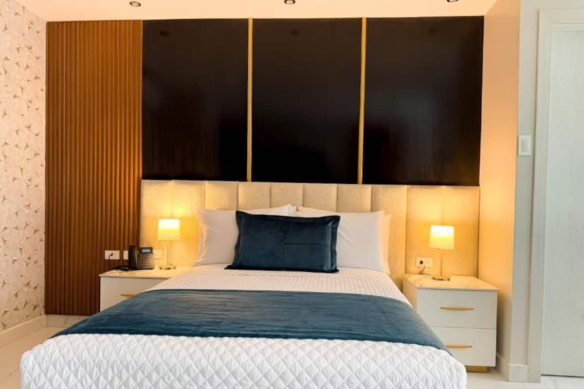Quarto moderno com uma cama grande, duas mesas de cabeceira e painel decorativo na parede.