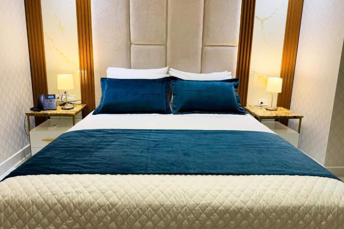Quarto de hotel com uma cama grande, duas mesas de cabeceira com luminárias e uma cabeceira acolchoada.