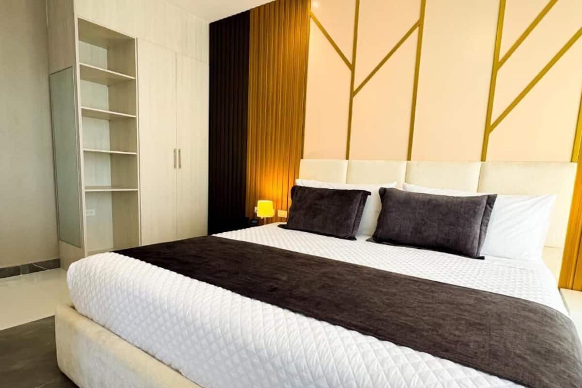 Quarto de hotel moderno com uma cama grande, um guarda-roupa e uma mesa de cabeceira com abajur.