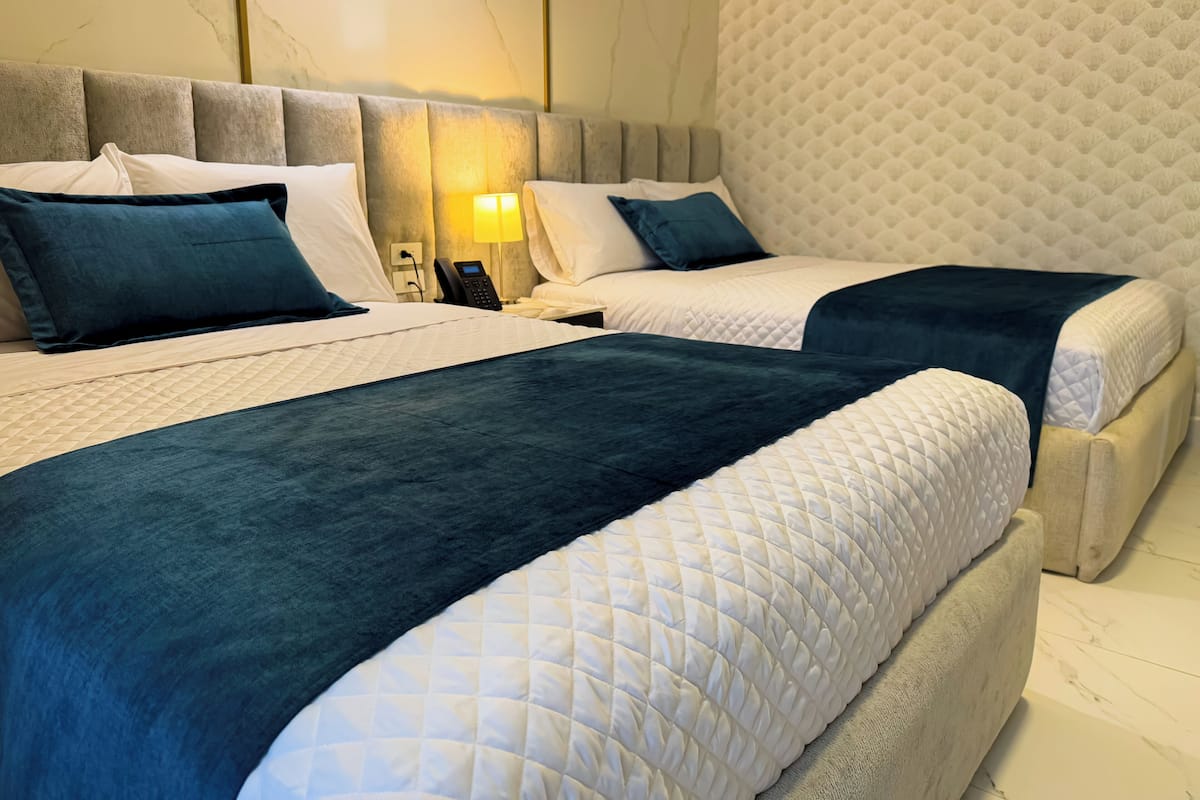 Quarto de hotel com duas camas, cada uma com um edredom acolchoado, uma mesa de cabeceira com abajur e telefone.