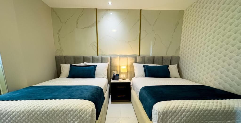 Een hotelkamer met twee bedden, een nachtkastje en een wand met een marmerachtig patroon.