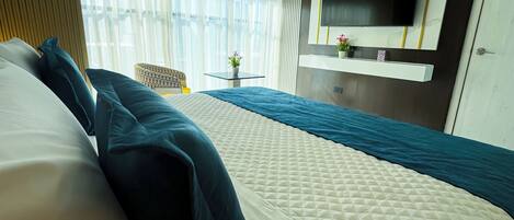 A hotel room with a large bed, a TV mounted on the wall, a small table with a plant, and a chair.