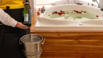 A person holding a bottle of wine next to a bathtub with rose petals.