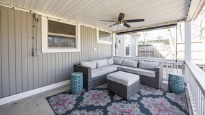 A covered porch with a sectional sofa, two ottomans, and a patterned rug. - Modern & Inviting Remodeled 3BR in Independence, KS! (Independence)