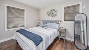 A bedroom with a bed, bedside lamps, a mirror, and a wall art piece. - Modern & Inviting Remodeled 3BR in Independence, KS! (Independence)