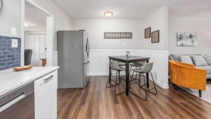 A modern kitchen with a built-in refrigerator, a dining area with a table and chairs, and a living area with a sofa and cushions. - Modern & Inviting Remodeled 3BR in Independence, KS! (Independence)