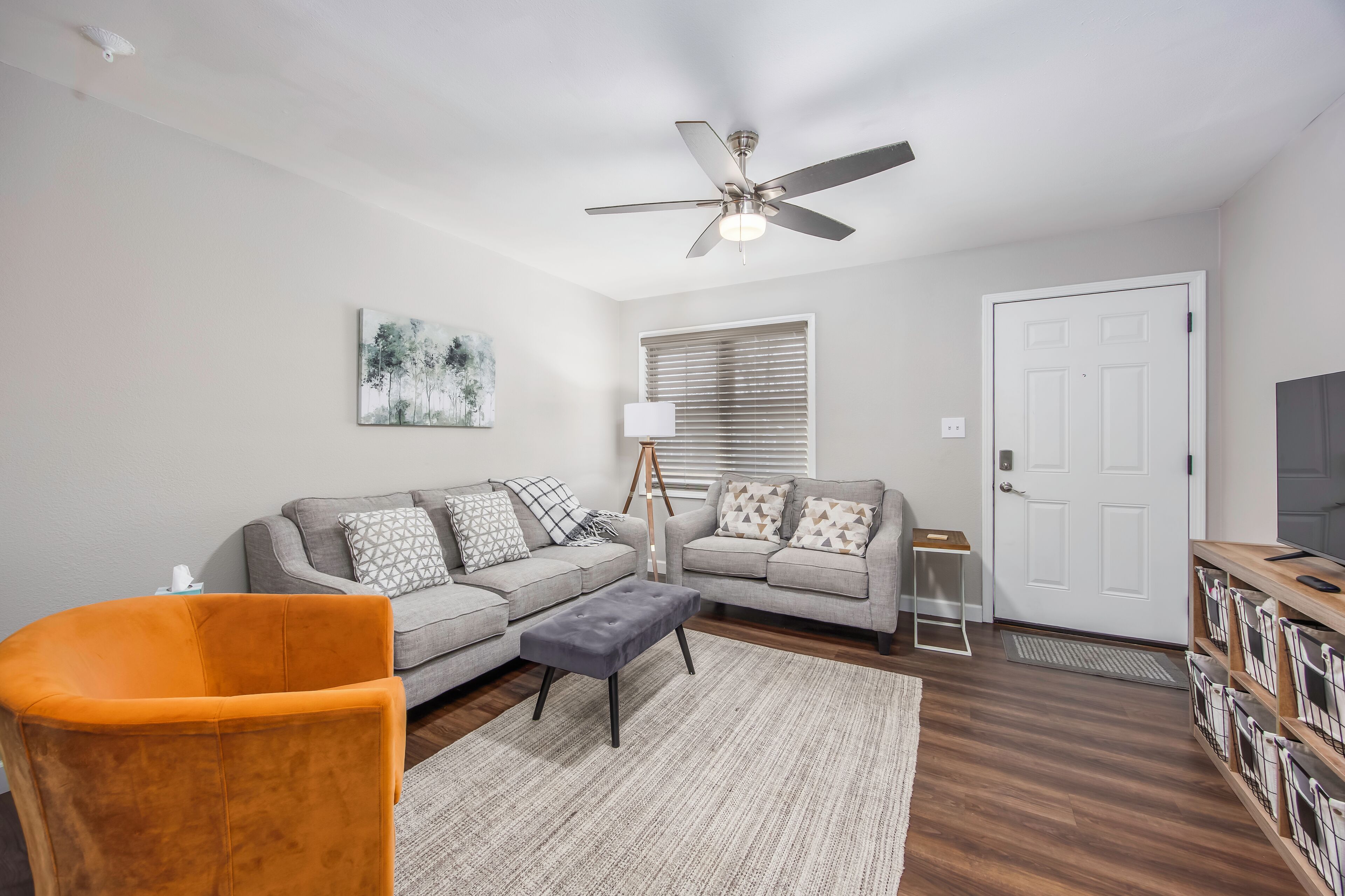 A living room with a grey sofa, orange armchair, and a ceiling fan.