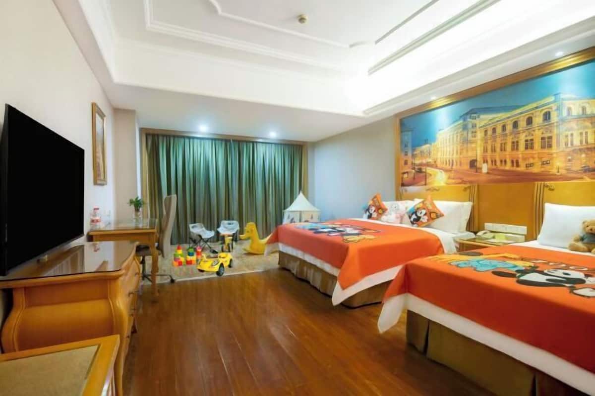 Habitación de hotel con dos camas, televisión, escritorio y un cuadro de un edificio.