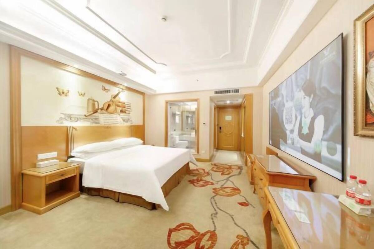 A hotel room with a bed, bedside table, TV, and a floral carpet.