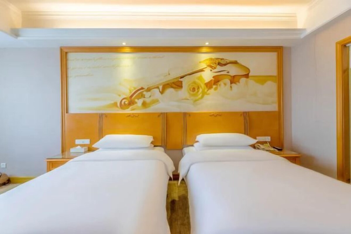 A hotel room with two beds, a large painting on the wall, and a wooden headboard.