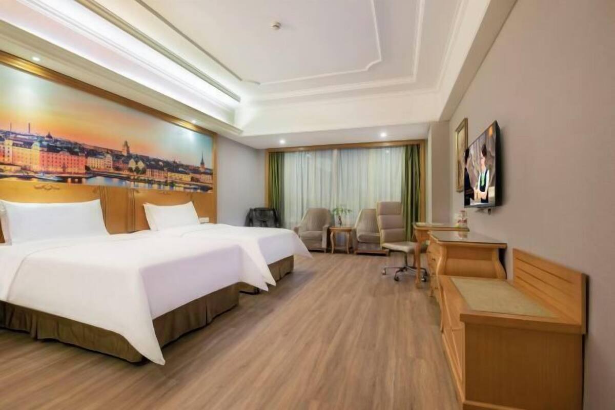 A hotel room with two beds, a desk, a chair, and a TV.