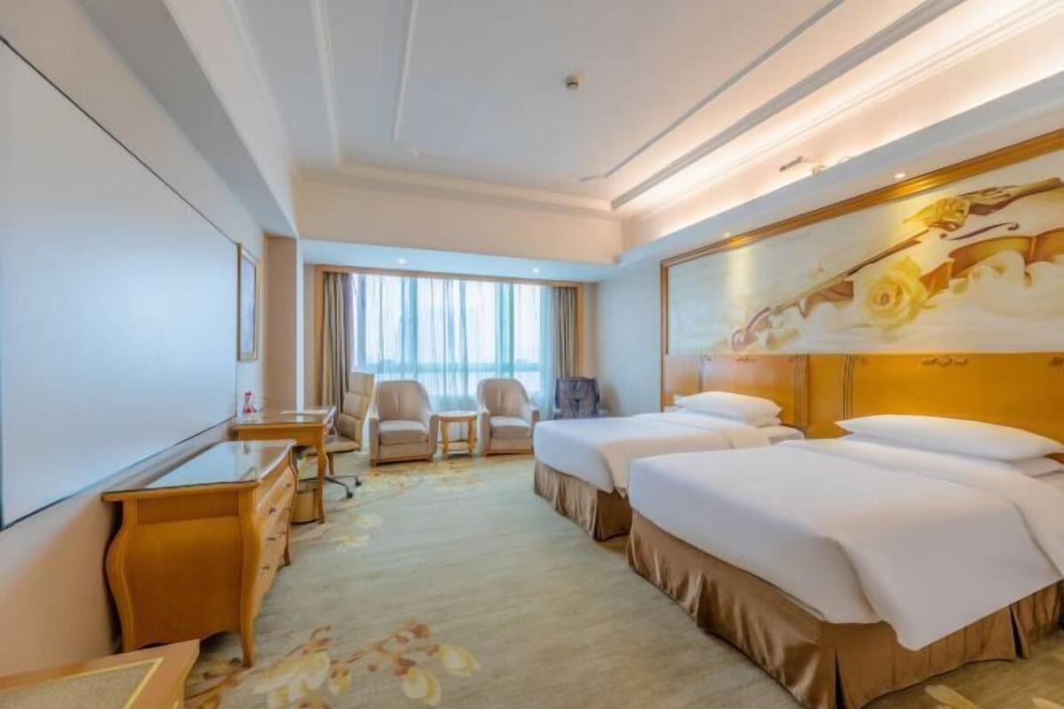A hotel room with a large bed, a desk, a chair, and a television.