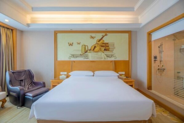 Quarto de hotel com cama, poltrona de massagem, obras de arte na parede e área de chuveiro.