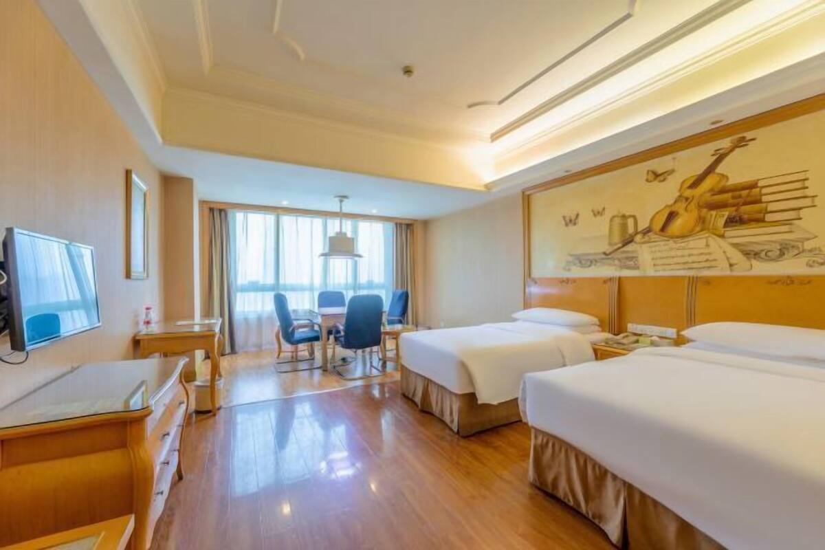 A hotel room with two beds, a desk, a chair, a television, and a large mural on the wall.