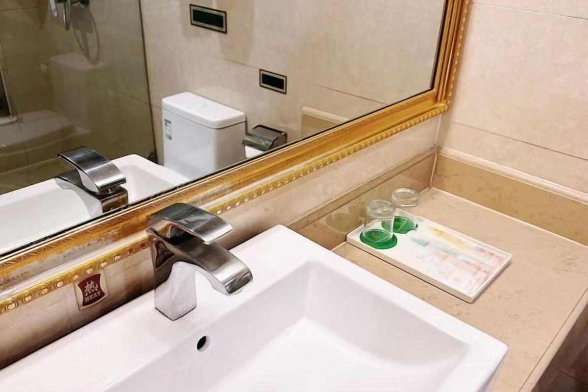 Um banheiro com uma pia branca, um espelho com moldura dourada e produtos de higiene no balcão.