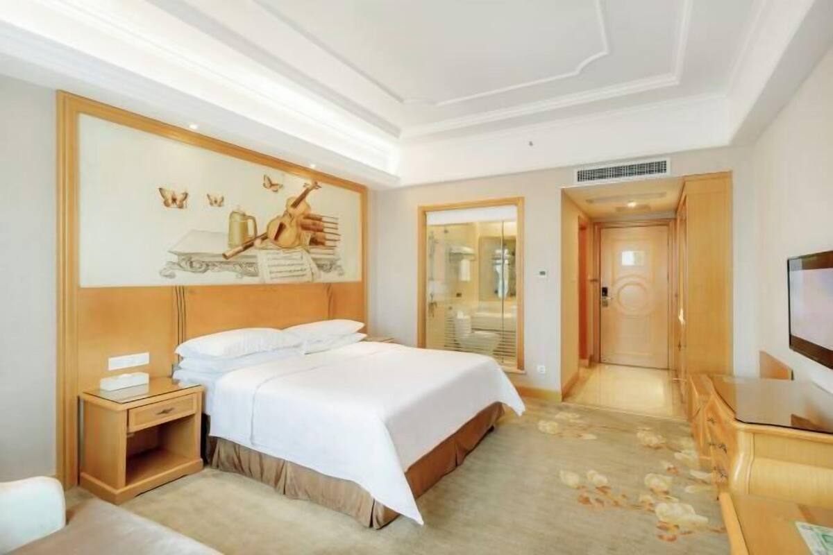 A hotel room with a bed, bedside table, TV, and a painting on the wall.