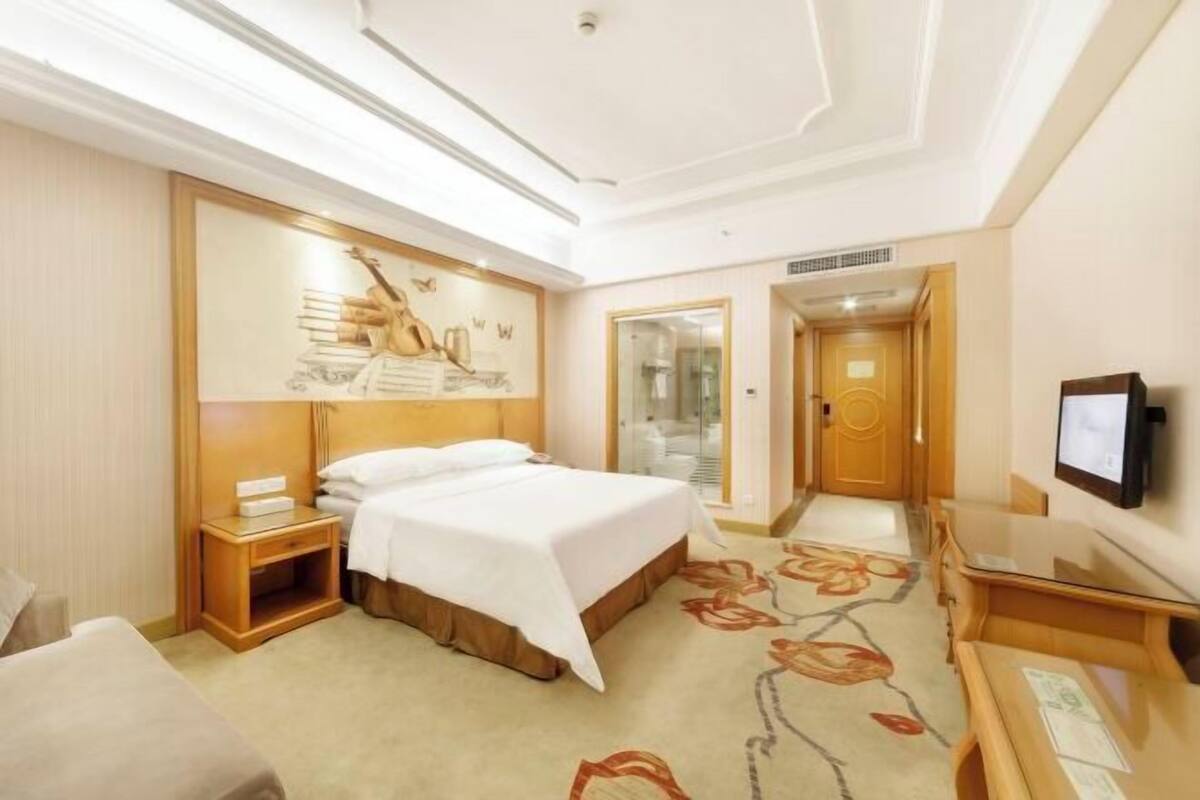 A hotel room with a bed, bedside table, a flat-screen TV, and a large painting on the wall.