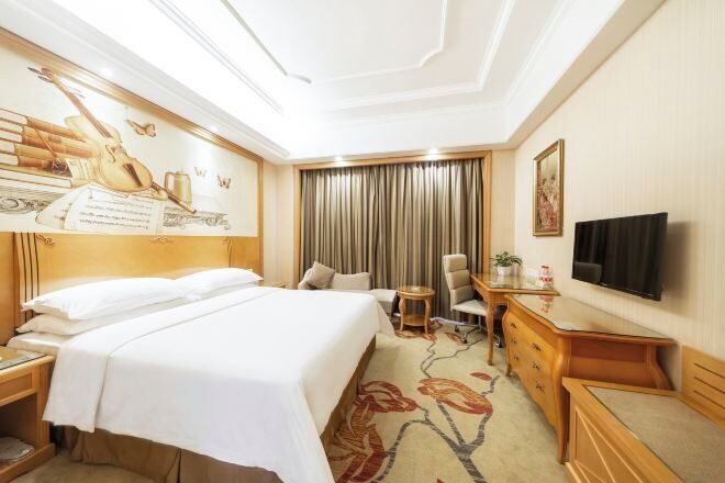 A hotel room with a bed, a desk, a chair, a television, and a large window with curtains.