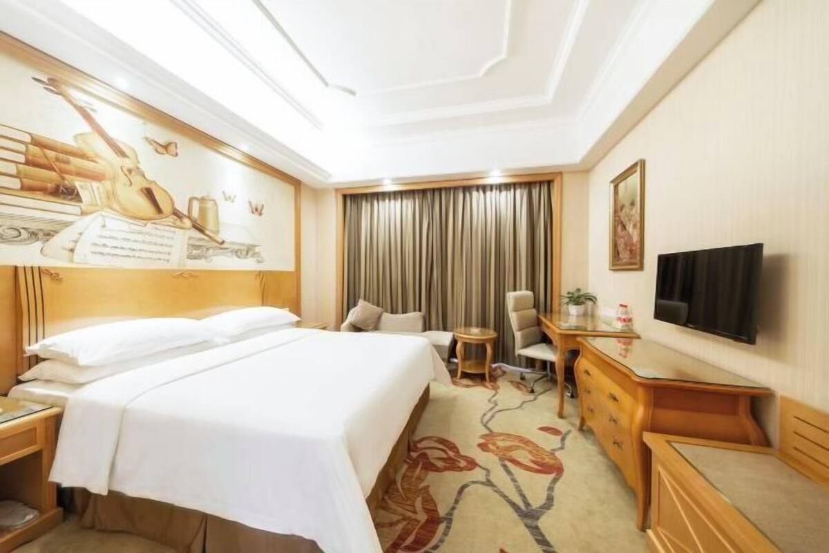 A hotel room with a bed, a desk, a chair, a television, and a large window with curtains.