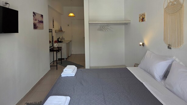 Habitació d'hotel amb un llit gran, un televisor de pantalla plana penjat a la pared, un escriptori amb cadira i un penjall de macramé.