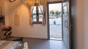 A room with a bed, a bedside table, a hanging dreamcatcher, and a window with curtains. - Calypso Heaven (Santorini)