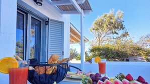 A breakfast setup with croissants, fruit, and juice on a balcony with a view of trees and a building. - Calypso Heaven (Santorini)
