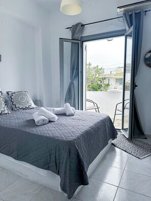 A bedroom with a bed, pillows, a towel, a window, and a door leading to a balcony. - Calypso Heaven (Santorini)