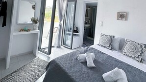 A modern bedroom with a large bed, a walk-in closet, a bathroom, and a view of the outdoors. - Calypso Heaven (Santorini)