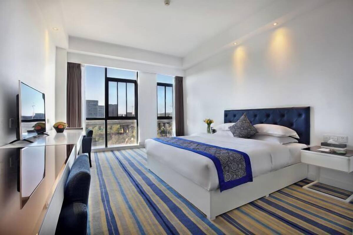 Habitación de hotel con una cama grande, un escritorio, una silla, un televisor y un balcón con vistas a la ciudad.