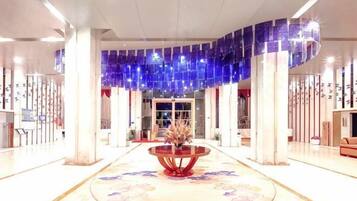 A spacious lobby with a central round table, a chandelier, and a reception desk.