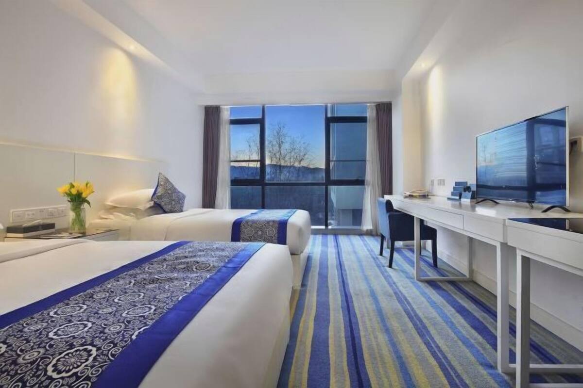 Habitación de hotel con dos camas, un escritorio, un televisor y un ventanal grande.