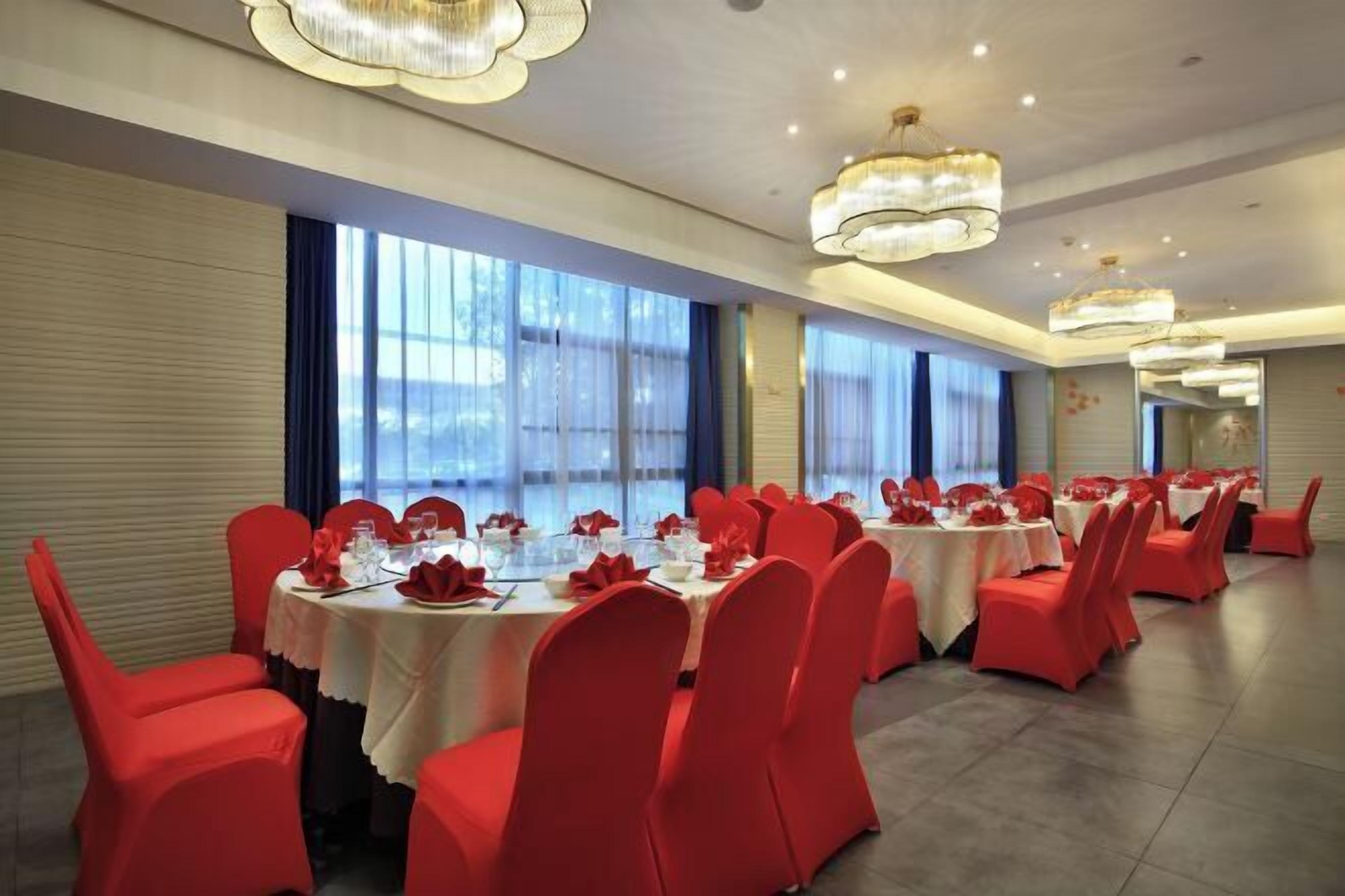 Une salle de banquet avec des tables rondes, des chaises rouges et des lustres.