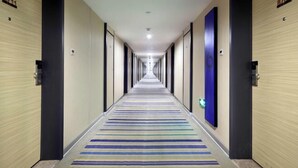 Ein langer, schmaler Hotelkorridor mit Streifenmuster-Teppich, Türen an beiden Seiten und einem blauen Notausgangsschild.