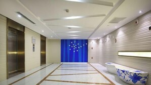 Eine moderne Hotelhalle mit Marmorboden, Aufzügen, einem Empfangsbereich mit blauem Blumendesign und einer blauen Wand mit weißen Vogelsilhouetten.
