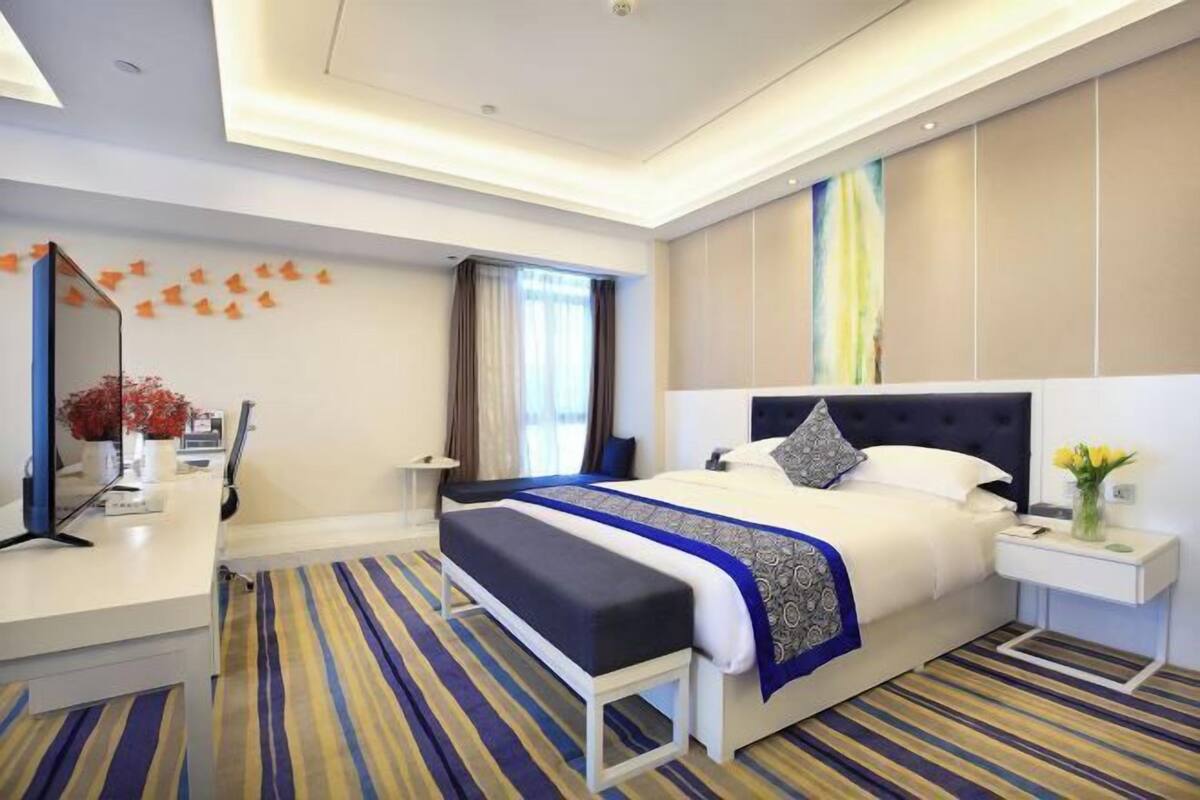 Una habitación de hotel con cama, mesitas de noche, un escritorio y un espejo.