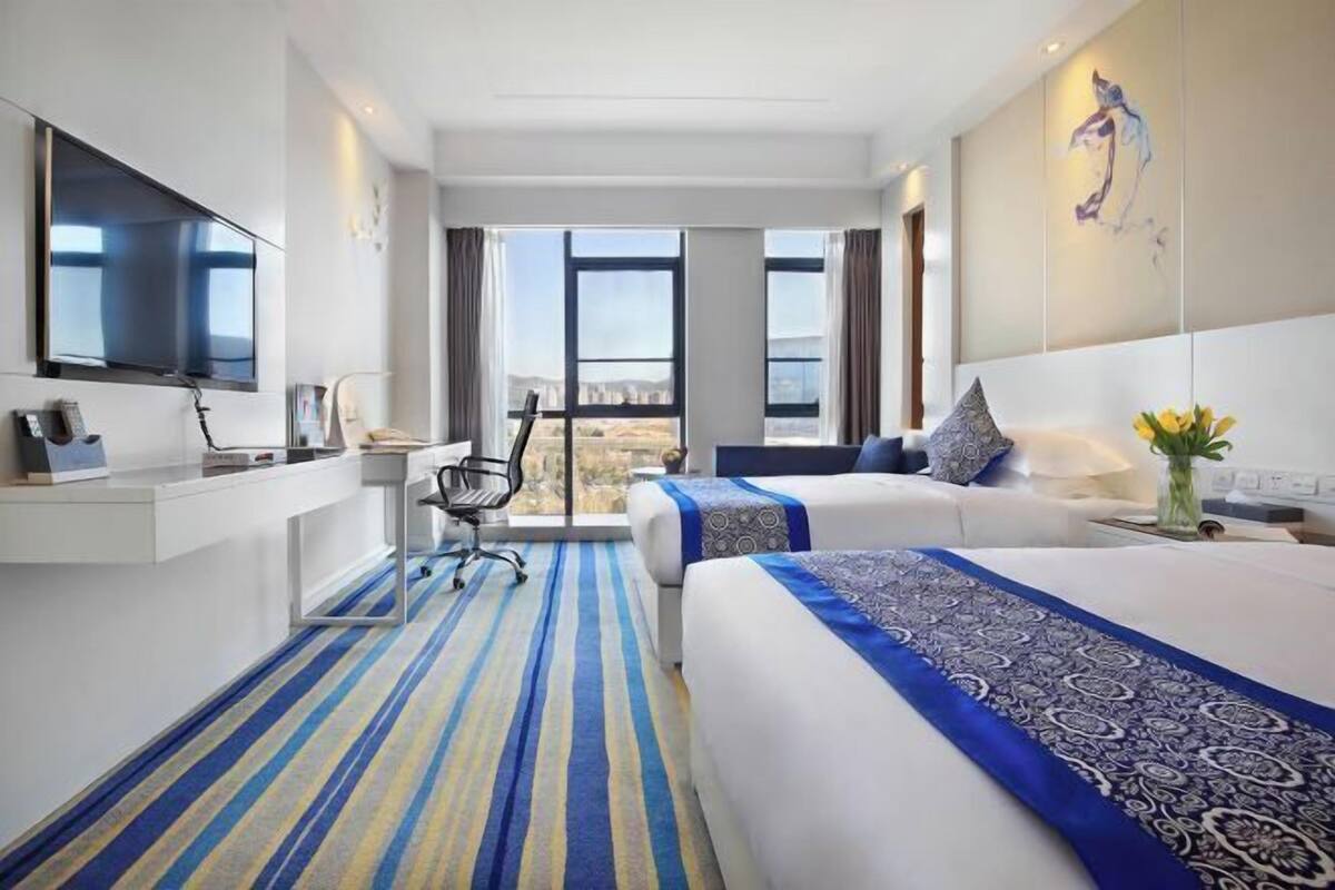 Habitación de hotel con una cama grande, un escritorio, una silla, un televisor y vistas a la ciudad.