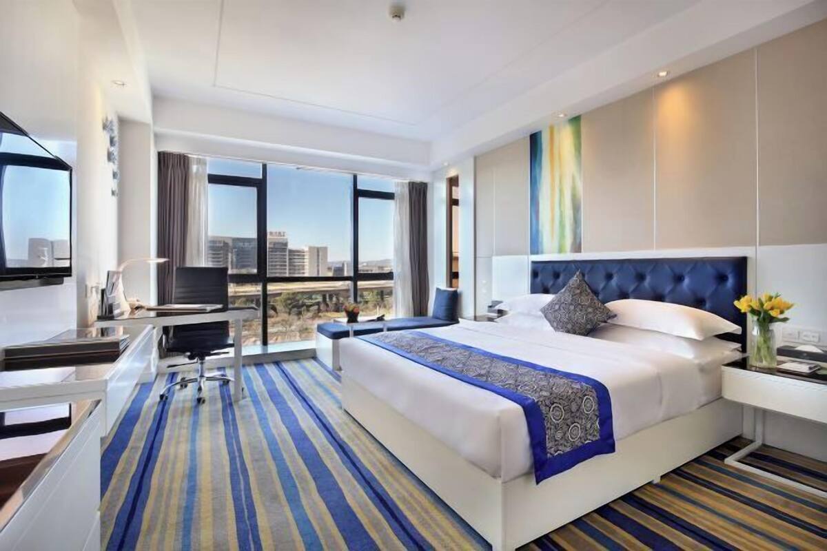 Habitación de hotel con una cama grande, un escritorio, una silla, un televisor y vistas a la ciudad.