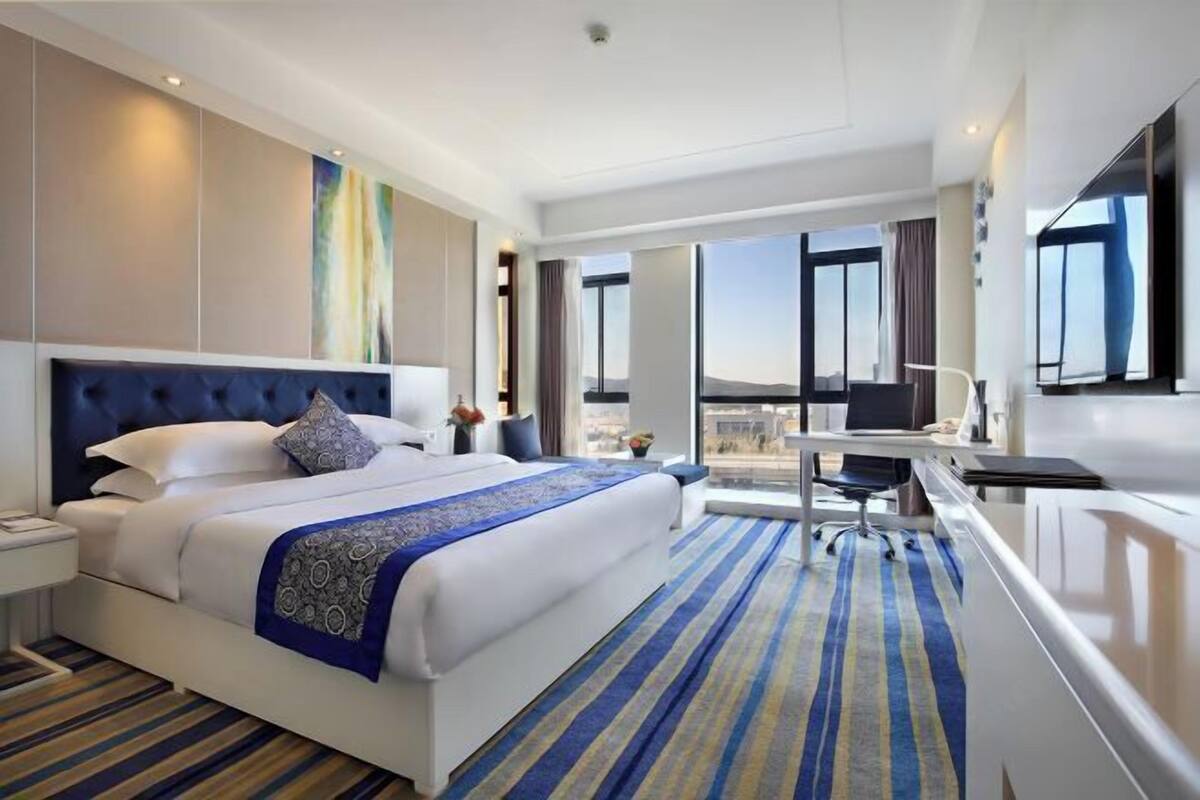Una habitación de hotel con una cama grande, un escritorio, una silla, una lámpara de escritorio, un teléfono y una ventana con vistas.